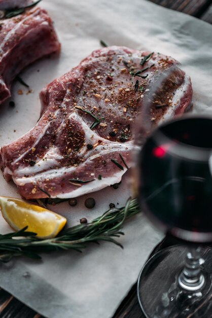 Glas Rotwein mit rohem Ribeye-Steak, dekoriert mit Rosmaringewürzen und Zitronenscheibe beim Backen