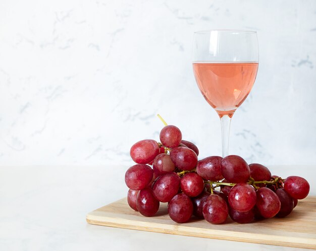 Glas Rotwein und Trauben auf einem Holzbrett.