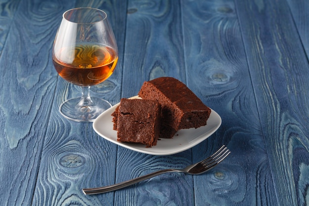 Glas Rum auf Holztablett mit Schokoladenbrownies im Hintergrund, selektiver Fokus