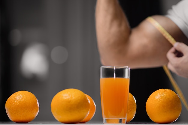 Glas Saft und Orangennahaufnahme auf eines Mannes, der sein Bizeps mit einem messenden Band misst