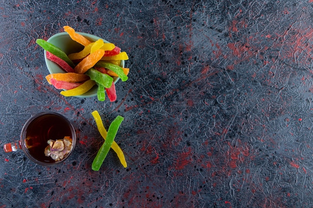 Glas schwarzer Tee mit Schüssel mit bunten Bonbons auf dunklem Hintergrund.