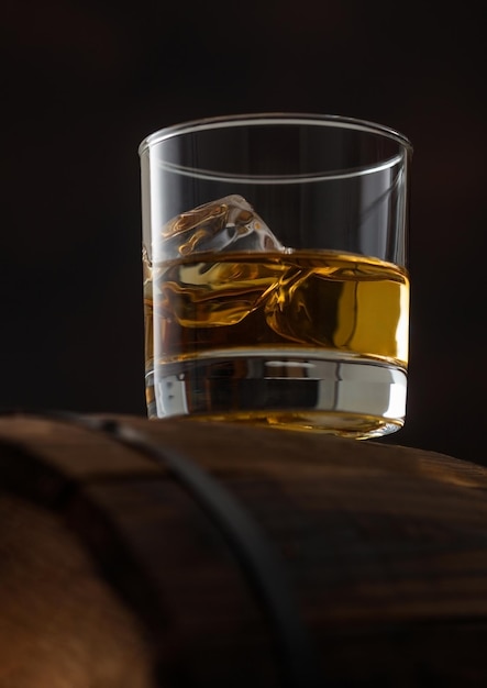 Foto glas single malt whisky mit eiswürfeln auf holzfass auf schwarzem hintergrund