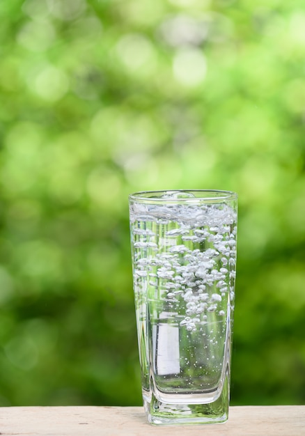 Glas Spritzwasser auf Holztisch mit grüner Natur