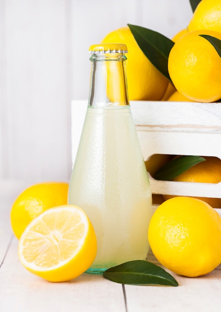 Glas und Flasche frischen Bio-Zitronensaft mit rohen Zitronen in weißer Holzkiste