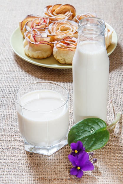 Glas und Flasche Milch, Teller mit hausgemachten Keksen in Form einer Rose auf Sackleinen