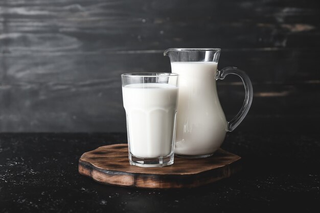 Glas und Krug leckere Milch auf dunklem Tisch