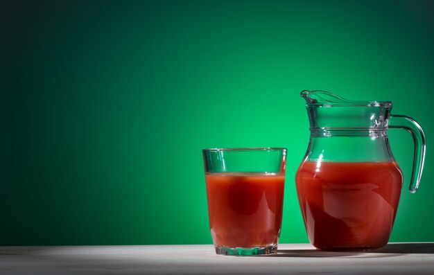 Glas und Krug Tomatensaft auf grün