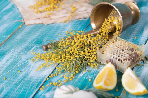 Glas Wasser, Mimosenblüten, Waben und Zitronenstücke auf einer Holzoberfläche. Nahaufnahme