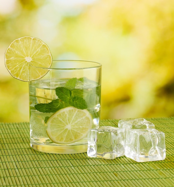 Glas Wasser mit Eisminze und Limette auf Tisch auf hellem Hintergrund