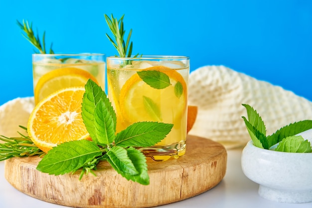 Glas Wasser mit Orangenminze und Rosmarin auf blauem Hintergrund