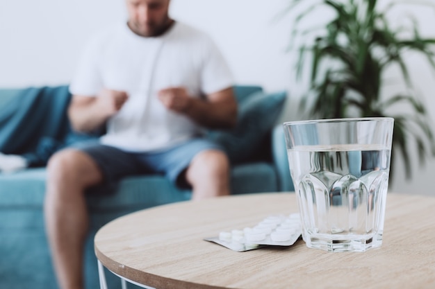 Glas Wasser mit Pillen auf dem Hintergrund der Person, die Temperatur misst