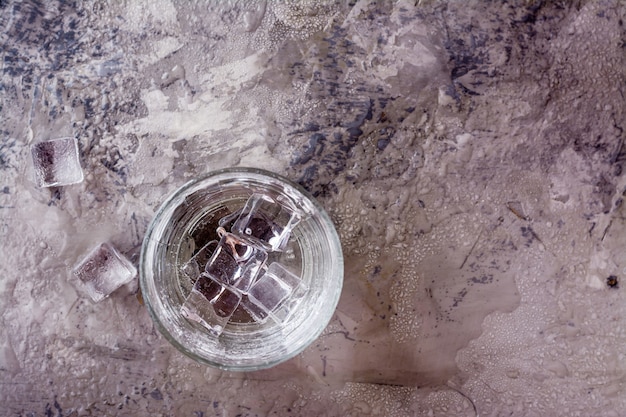 Glas Wasser spritzte mit Tropfen und Stücken Eis auf einer grauen Tabelle