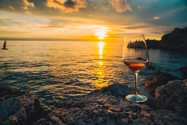 Glas Wein am felsigen Meeresstrand bei Sonnenuntergang