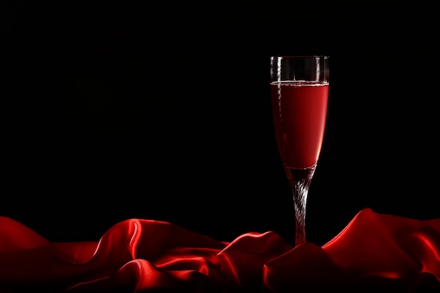 Glas Wein auf roter Seide mit dunklem Hintergrund