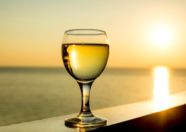 Glas Weißwein auf einem Sonnenuntergangshintergrund im Meer