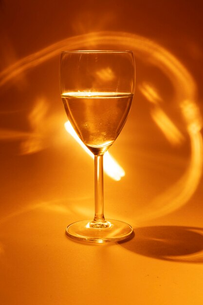 Glas Weißwein auf orangem Hintergrund mit Lichtern und Glitzern