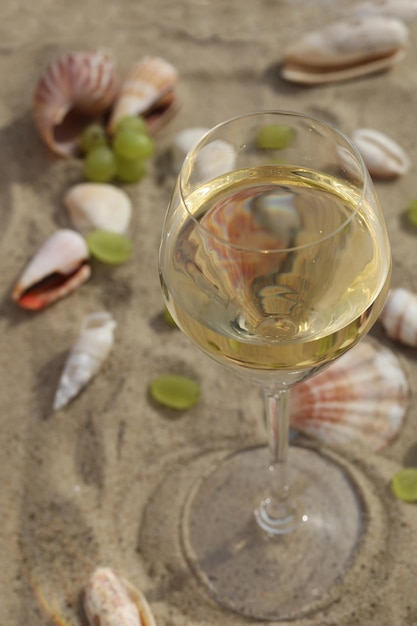 Glas Weißwein auf Sand als Hintergrund mit Muscheln