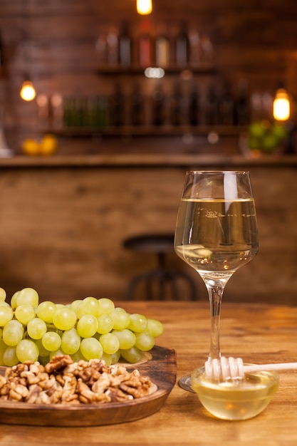 Glas Weißwein mit frischen Trauben und Wollnüssen auf einer Holzplatte in einem Vintage-Restaurant. Französischer Wein. Weinfest.