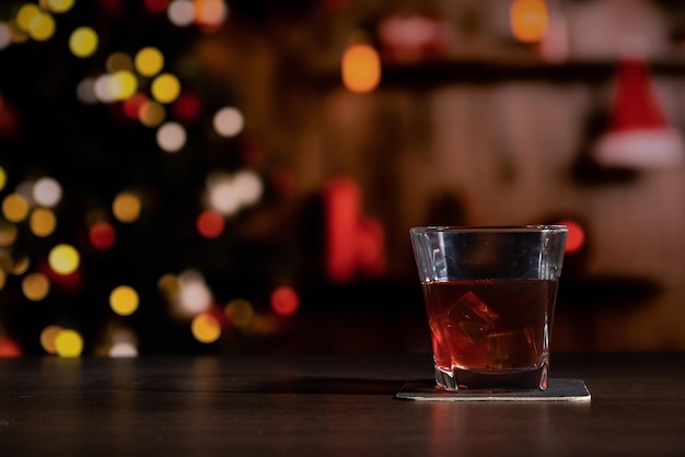 Glas Whiskey an der Bar vor dem verschwommenen Bild Weihnachtszimmer mit Baum und festlicher Bokeh-Beleuchtung verschwommener Urlaubs-Hintergrund