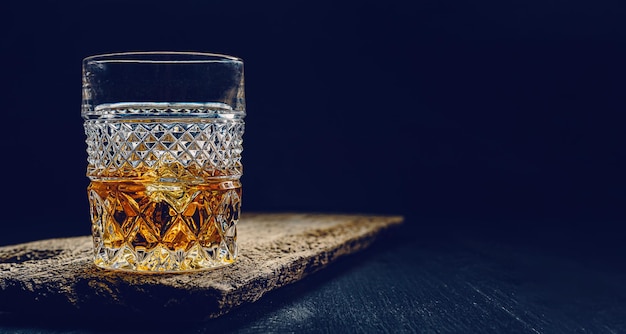 Glas Whiskey mit Eis auf einem Holztisch, umgeben von Rauch