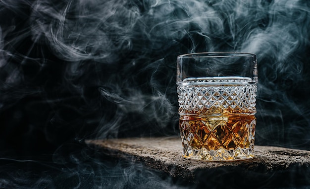 Glas Whiskey mit Eis auf einem Holztisch, umgeben von Rauch