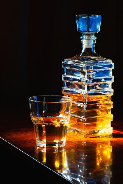 Glas Whisky mit alter quadratischer Karaffe auf einem lackierten Holztisch