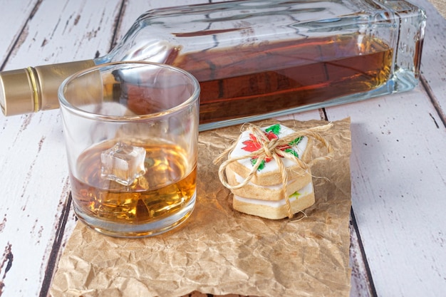 Glas Whisky mit Eis auf braunem Papier neben Keksen mit Sisalschleife.