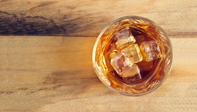 Glas Whisky mit Eis auf hölzernem Hintergrund