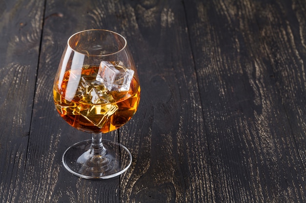 Glas Whisky mit Eiswürfeln auf Holzbrettern serviert. Vintage Arbeitsplatte mit Highlight und einem Glas Schnaps