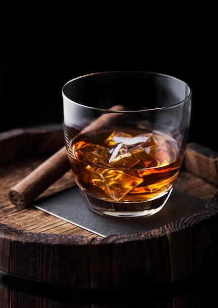 Glas Whisky mit Eiswürfeln und Zigarre auf Holzfass
