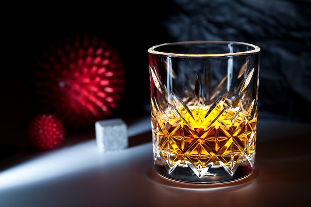 Glas Whisky oder Brandy auf dunklem Hintergrund neben dem abstrakten Modell des Virusstamms. Trunkenheit.