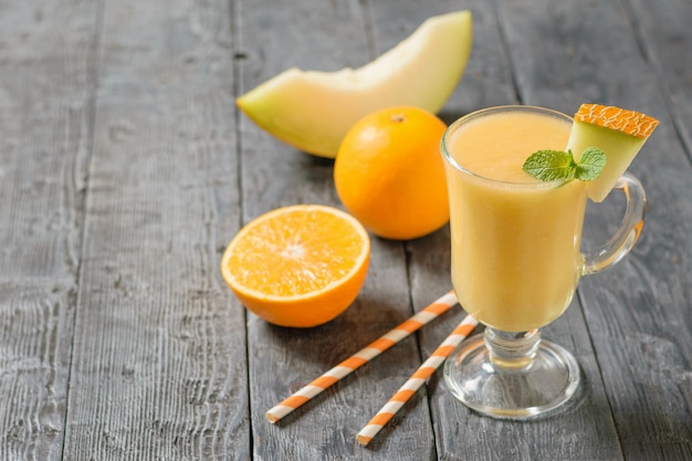 Glasbecher mit einem Smoothie aus Melone, Cocktailröllchen und Orangenscheiben auf rustikalem Tisch