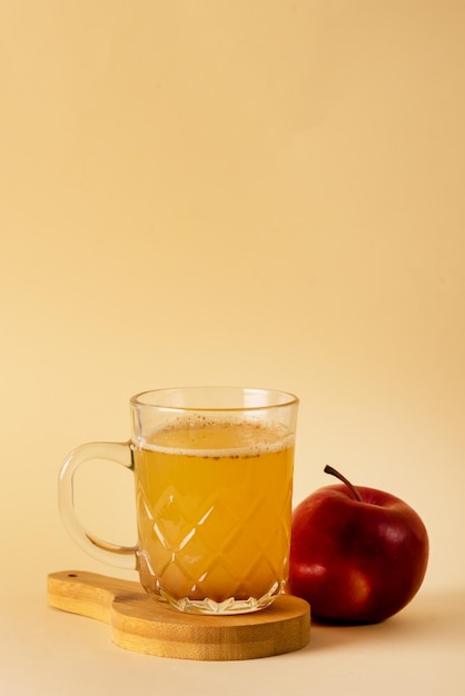 Glasbecher mit frischem Bio-Apfelwein mit zimtgelbem Hintergrund vertikal