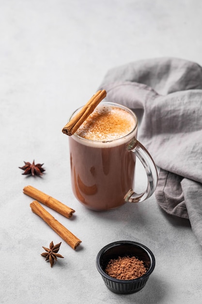 Glasbecher mit heißer Schokolade und Milchschaum auf einem hellen Hintergrund mit Zimtstäbchen, Anisstern und Kakaopulver