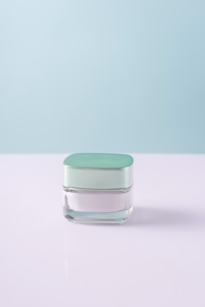 Glasbehälter mit kosmetischer weißer Creme auf einem minimalistischen weißblauen Hintergrund