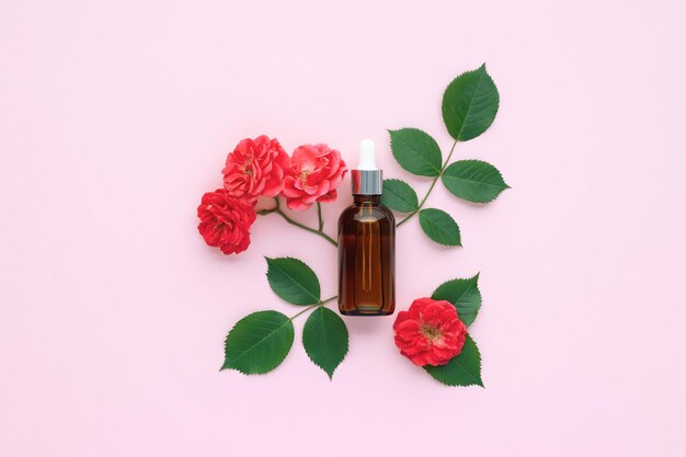 Glasfläschchen mit Pipette und Rose auf rosa Papier Hintergrund Top-View Gesichtsmassageöl Aromatherapie-Konzept Blumenduft Flachlage-Komposition mit Blumen und Blättern Hautpflege-Naturprodukt