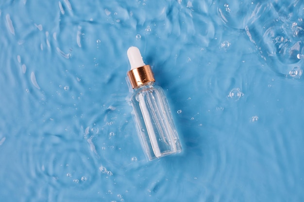 Glasflasche Anti-Aging-Serum und fallende Wassertropfen auf blauem Hintergrund
