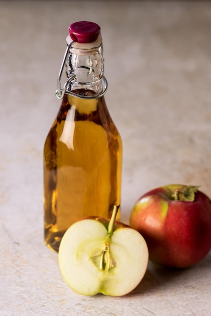 Glasflasche mit Apfelessig und Apfel auf konkretem Hintergrund Vertikale rohe rote Äpfel