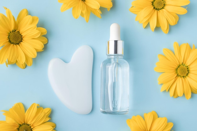 Glasflasche mit Öl Gua sha Stein für Gesichtsmassage auf blauem Hintergrund mit Blume Kosmetische Gesichtspflege und Spa Natürliches Behandlungskonzept