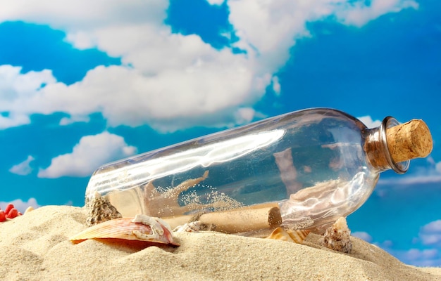 Glasflasche mit Notiz im Inneren auf Sand auf blauem Himmelshintergrund