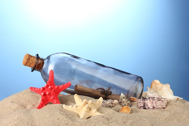 Glasflasche mit Notiz im Inneren auf Sand auf blauem Hintergrund