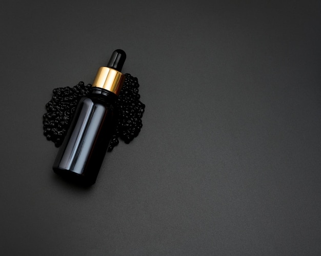 Glasflasche mit Pipette liegt auf einem Haufen schwarzen Kaviars, schwarzer Hintergrund. Natürliche Komik. Produktbranding, Draufsicht