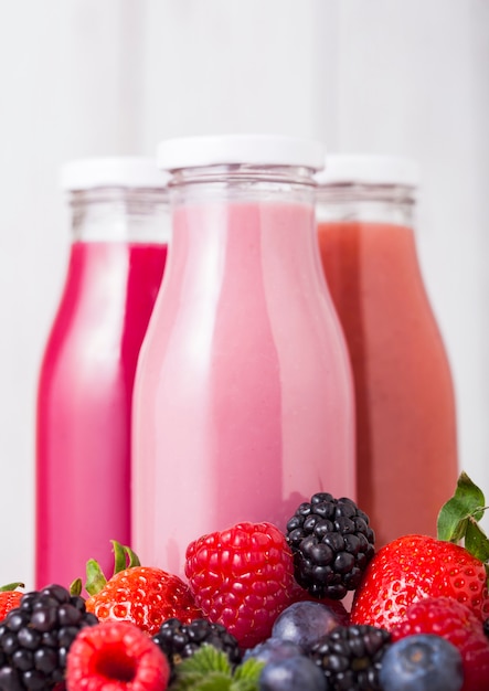 Glasflaschen mit frischem Sommerbeeren-Smoothie auf Holztisch. Erdbeeren und Himbeeren mit Blaubeeren und Brombeeren.