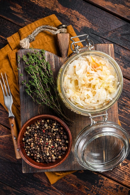 Glasgefäß mit hausgemachtem Sauerkraut, schwarzem Pfeffer und Thymian Holzhintergrund Draufsicht