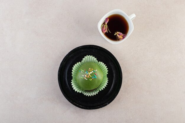 Glasierter Cupcake mit Streuseln und Tasse Tee auf Steintisch.