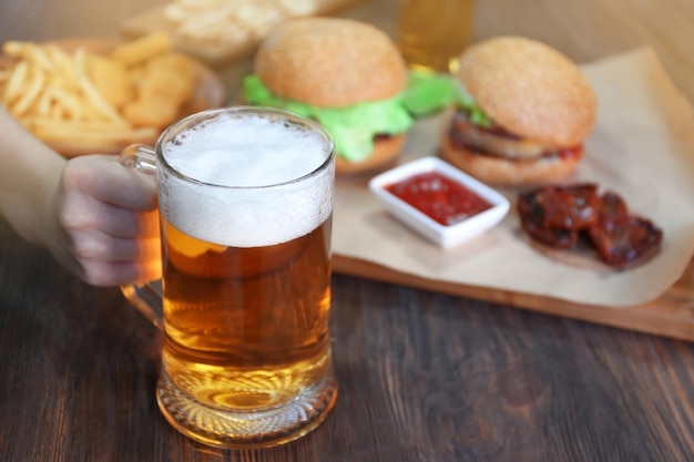 Glaskrug helles Bier mit Snacks auf dunklem Holztisch aus nächster Nähe