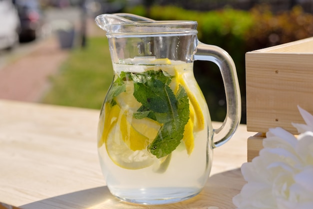 Glaskrug mit frischer kühler hausgemachter Limonade, die auf hölzernem Marktstand an sonnigem Tag in natürlicher Umgebung steht