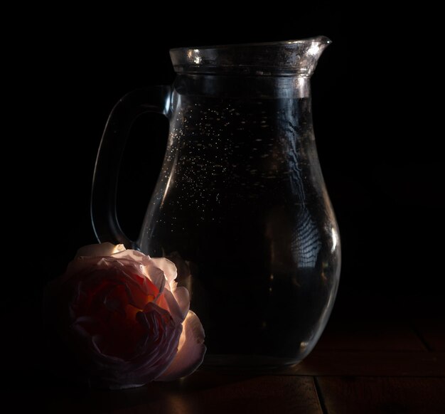 Glaskrug mit Wasser auf dunklem Hintergrund mit Rose
