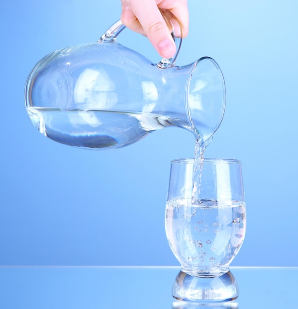 Glaskrug mit Wasser und Glas auf blauem Hintergrund