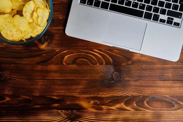 Glasplatte mit Chips neben einem Laptop auf einem verbrannten hölzernen Hintergrund. Speicherplatz kopieren.